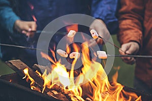 Hands of friends roasting marshmallows over the fire in a grill