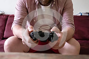 hands with gamepad of man sitting on sofa and playing video games