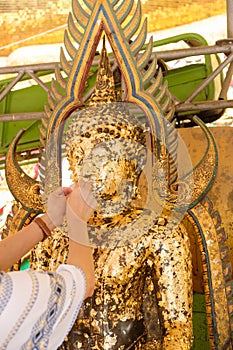 hands gilding gold leaf onto the Buddha statue image.Which people use to worship the Buddha image.