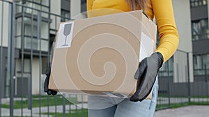 Hands Of Girl Carrying Box. She Is Wearing Gloves. Delivery Worker. Face Invisible. She Goes And Carries Box On The