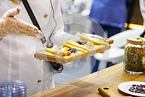 Hands of girl with cheeses on wooden plate. Inviting and offer to customers to test products