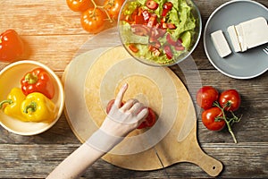 Hands of a girl cut tomates on a table, the process of making vegetarian salad, close-up cutting of vegetables and greens