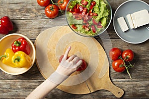 Hands of a girl cut tomates on a wooden table, the process of making vegetarian salad, close-up cutting of vegetables
