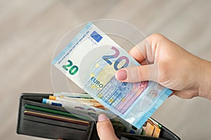 Hands of a girl holding 20 euro bill and wallet full of money, close up