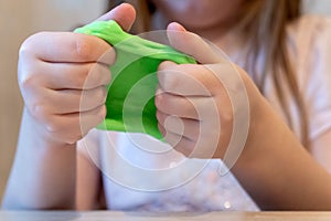 Hands of a girl holding a green slime. Slime in hands close-up. The child plays a slime, stretches it. Creative toy for