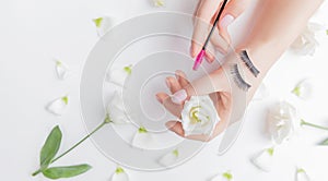 Hands girl master eyelash extension on white flowers background with pink brush, top view. Beauty concept