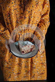 In the hands of a girl in an orange dress on a black plate is a piece of cake.