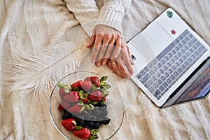 Hands girl with a plate of strawberries and blackberries in bed