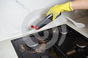 The hands of a girl in yellow gloves apply an anti-grease product to a gas stove with soot and dirt. Cleaning company