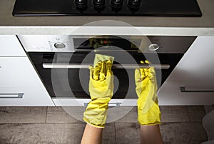 The hands of a girl in yellow gloves with a sponge wash a modern electric oven. Concept for cleaning grease stains