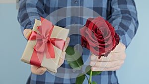 Hands are giving wrapped gift present with tied red bow, moves towards camera, close up. Man is holding little gift box and rose i