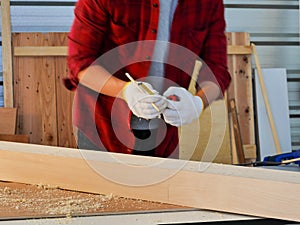 Hands with glove of  carpenter with red shirt  in workshop store working on wood plank and measurement tools work from home