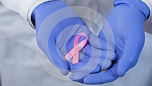 Hands in gloves carefully holds pink ribbon, symbol of breast cancer awareness