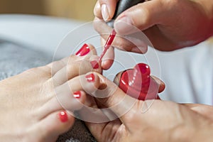 Hands in gloves cares about a woman`s foot nails. Pedicure, manicure beauty salon concept. Nail varnishing in red color.