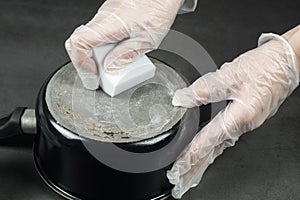 Hands in gloves cleaning old pot with eco friendly magic sponge