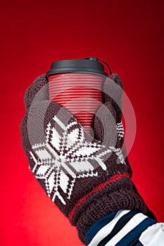 Hands with gloves & holding cup of hotdrink on a red background vertical composition