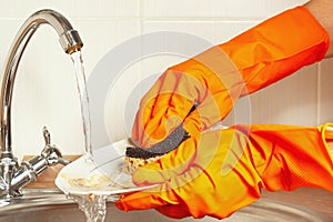 Hands in gloves wash the dishes under running water in kitchen