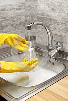 Hands in gloves washing drinking glass under running tap water