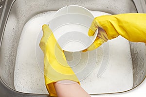 Hands in gloves washing white bowl under running tap water