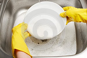 Hands in gloves washing white plate under running tap water