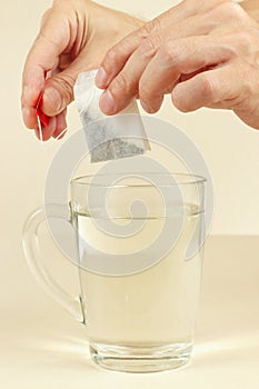 Hands are going to brew a tea bag in cup of hot water