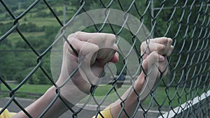Hands grab and shake the mesh fence clenching fists. Man protests against imprisonment and injustice