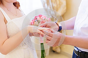 the hands of the groom put the wedding ring on the hands of their bride in the registry office close-up