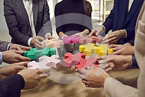 Hands of a group of business people assembling jigsaw puzzle. Cooperation, teamwork support concept