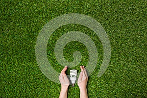 Hands guarding energy saving eco lamp over grass