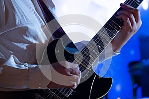 Hands guitarist on the strings. A man in a white shirt plays a black electric guitar. Musical theme. Blue background