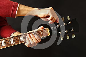 Hands of guitarist tunes the guitar on dark background