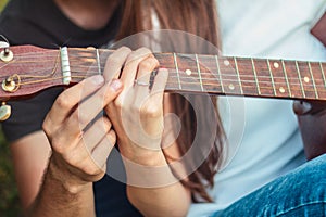 Hands of a guy and a girl on a guitar fretboard, learns to play the guitar