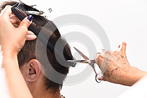 Hands of a hair stylist trimming hair with a comb and scissors