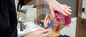 Hands of hairdresser combing hair making short pink hairstyle for a young caucasian woman in a beauty salon.