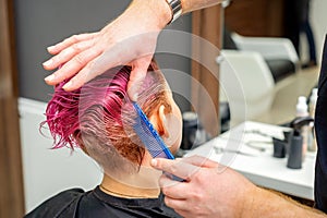 Hands of hairdresser combing hair making short pink hairstyle for a young caucasian woman in a beauty salon.