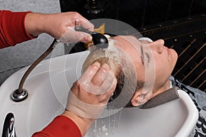 The hands of a hairdresser employee wash the hair and head of a young handsome guy of a client with rain before a haircut