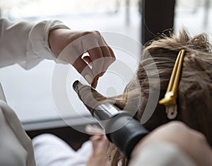 Hands of a hairdresser who winds a lock of hair on a curling iron