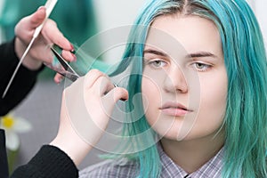 Hands of hairstylist cut hair of beauty woman with long green hair using scissors