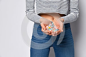 Hands with a handful of a variety of multi-colored drugs pills tablets on the background of female legs