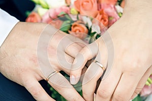 Hands of happy newly-married couple with gold wedding rings and flowers