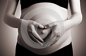 Hands in heart shape on belly of pregnant woman