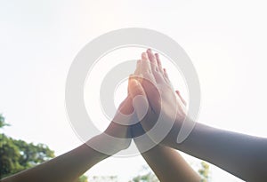 Hands hit and bumping together with sun light on sky background.