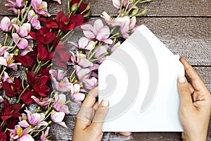 Hands hold a blank card mock-up, blank template above flowers on wood table for mother`s o women`s day concept