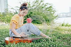 Hands hold coffee cup and write notes,lyrics in the book on quitar beside the sea and building city background photo