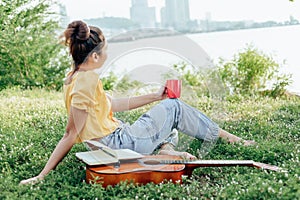 Hands hold coffee cup and write notes,lyrics in the book on quitar beside the sea and building city background photo