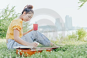 Hands hold coffee cup and write notes,lyrics in the book on quitar beside the sea and building city background photo