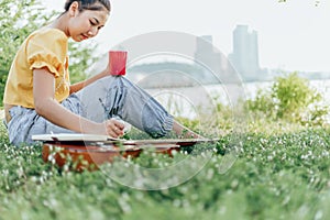 Hands hold coffee cup and write notes,lyrics in the book on quitar beside the sea and building city background photo