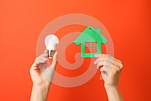 Hands hold energy saving bulb and house on red background