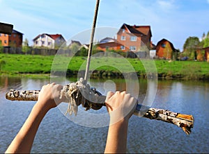 Hands hold rope swing before jump into the water on the lake and mansion hous background