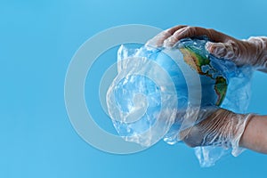 Hands hold a globe in a plastic bag on a blue background. Copy space